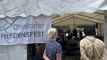 Blick von hinten ins Friedenszelt. Schauspieler*innen warten auf ihren Einsatz